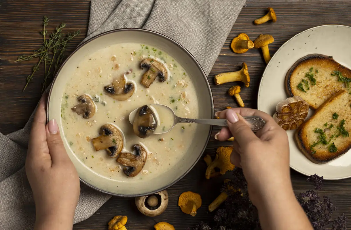 Cuenco de crema de champiñones con trozos enteros, acompañado de pan tostado con ajo y perejil sobre una mesa rústica.